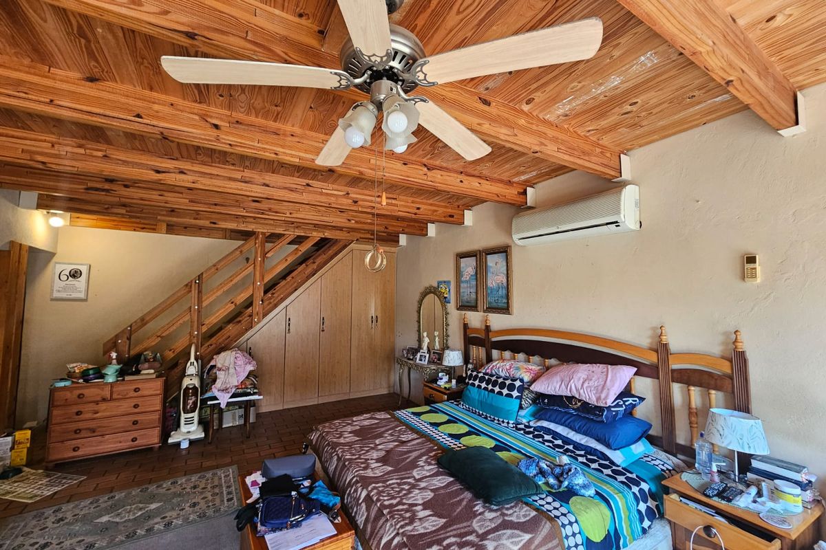 Spacious bedroom featuring a rustic exposed timber ceiling, built-in storage under the staircase, and a split-system air conditioner for climate control.