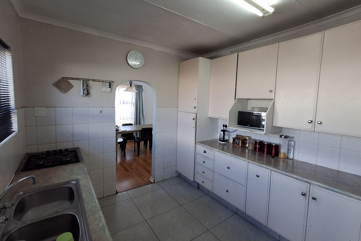 A functional kitchen featuring built-in cabinetry, laminate countertops, a gas hob, and a double bowl sink, with an arched doorway leading to the dining area.