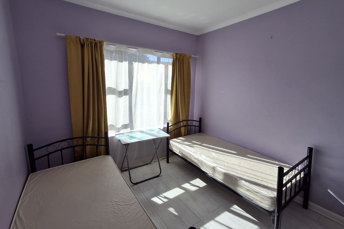 A simple bedroom featuring light-toned laminate flooring and purple painted walls, providing a functional space with natural light.