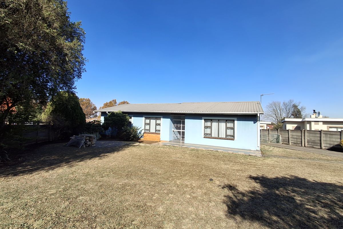 Rear view of the property featuring a metal roof, security gate, paved patio area, and a spacious garden with perimeter fencing.