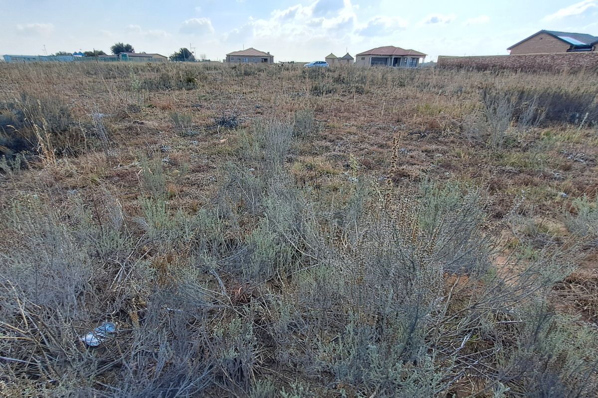 A wide-angle view of a vacant residential plot featuring natural vegetation and surrounding neighborhood development.