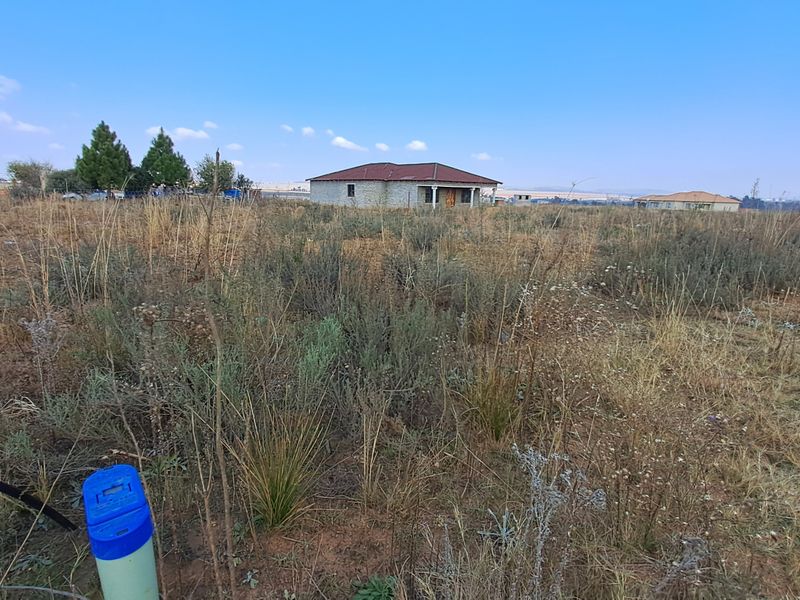 A wide-angle view of a vacant residential plot featuring natural vegetation and open space, with neighboring structures visible in the distance.