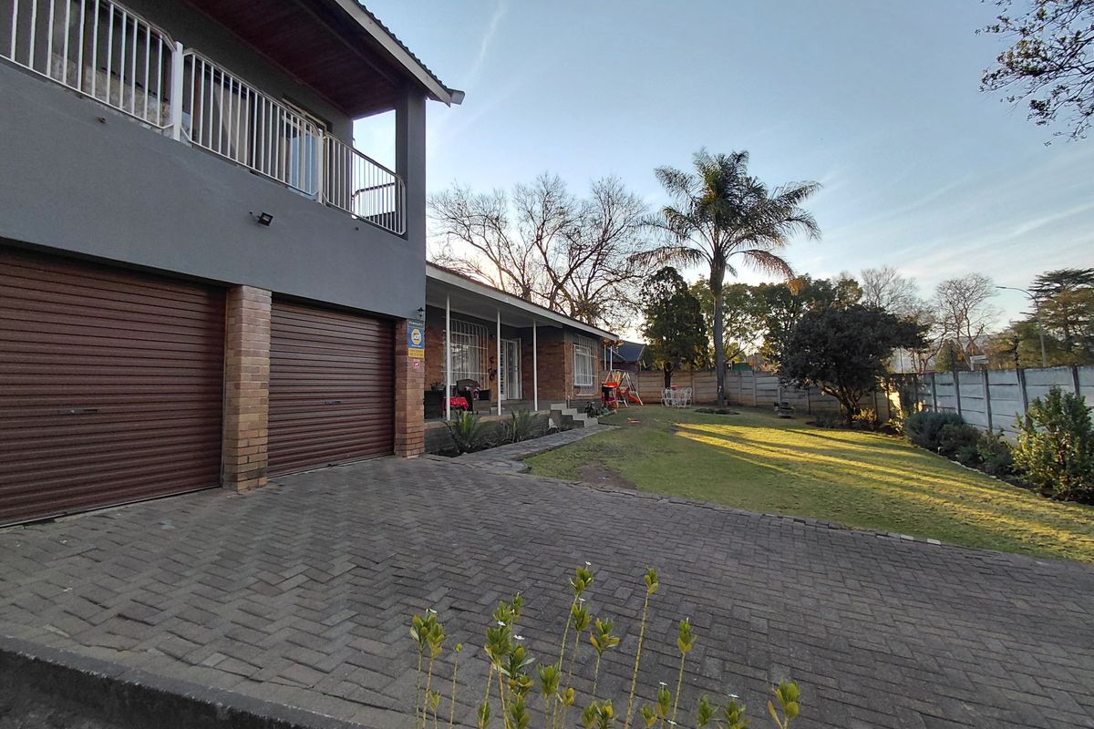 Rear view of the property featuring a paved driveway, double garage, upper-level balcony, and a spacious garden with perimeter walling.