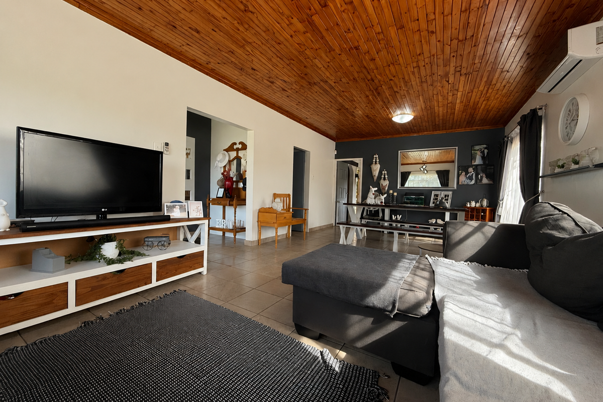 Spacious living room featuring a warm timber tongue and groove ceiling, neutral walls, and durable ceramic floor tiles with an integrated air conditioning unit.