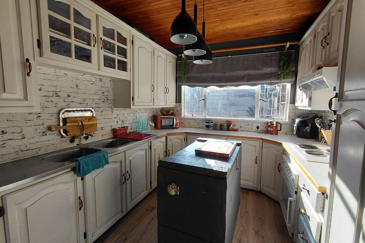 A functional kitchen featuring built-in cabinetry, a double sink, electric hob, extractor fan, and a distinctive timber-paneled ceiling.