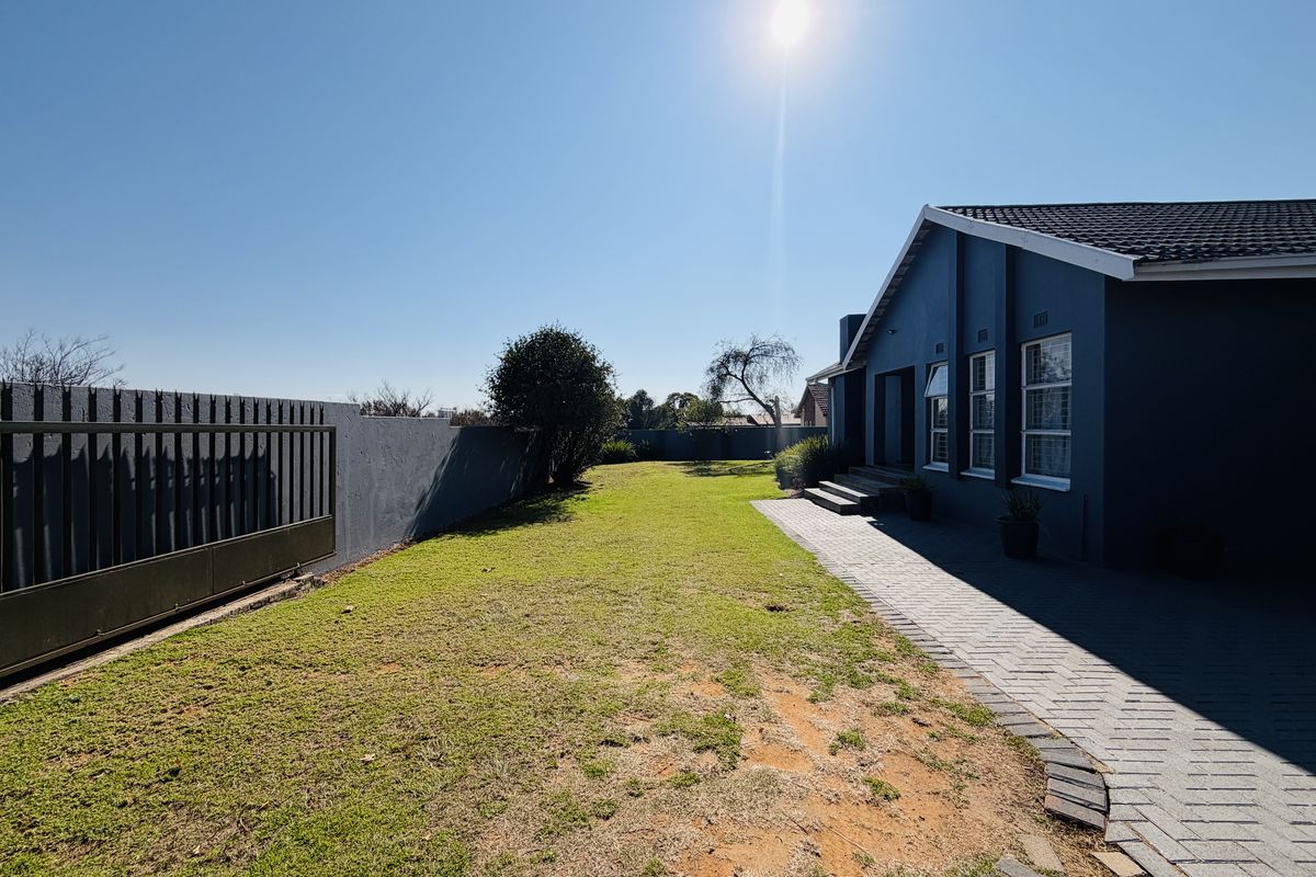 Rear exterior view of the property featuring a paved walkway, lawn area, and secure boundary wall with a metal gate.