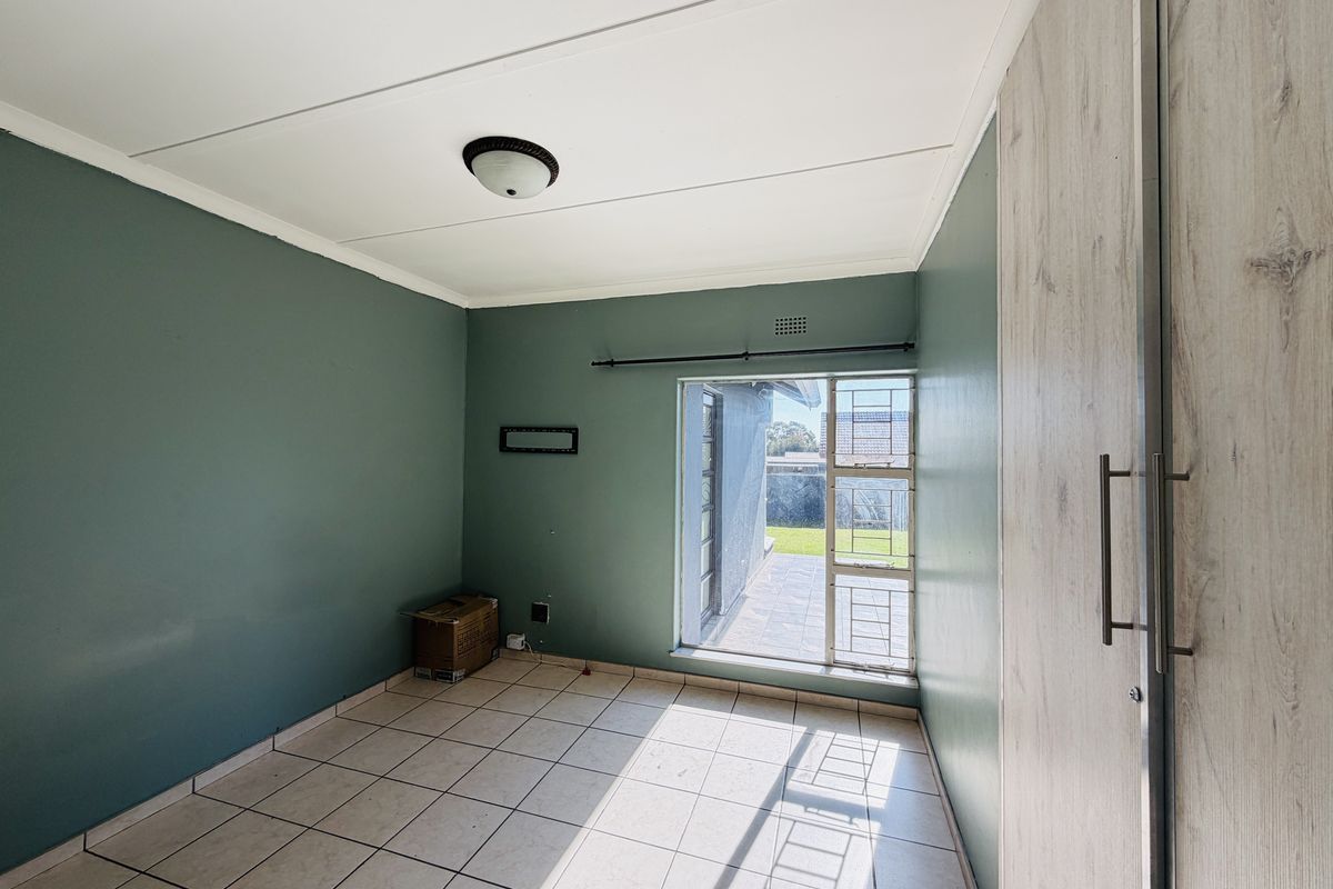 An empty bedroom featuring tiled flooring, a built-in wardrobe, and a window with security bars providing access to the exterior.
