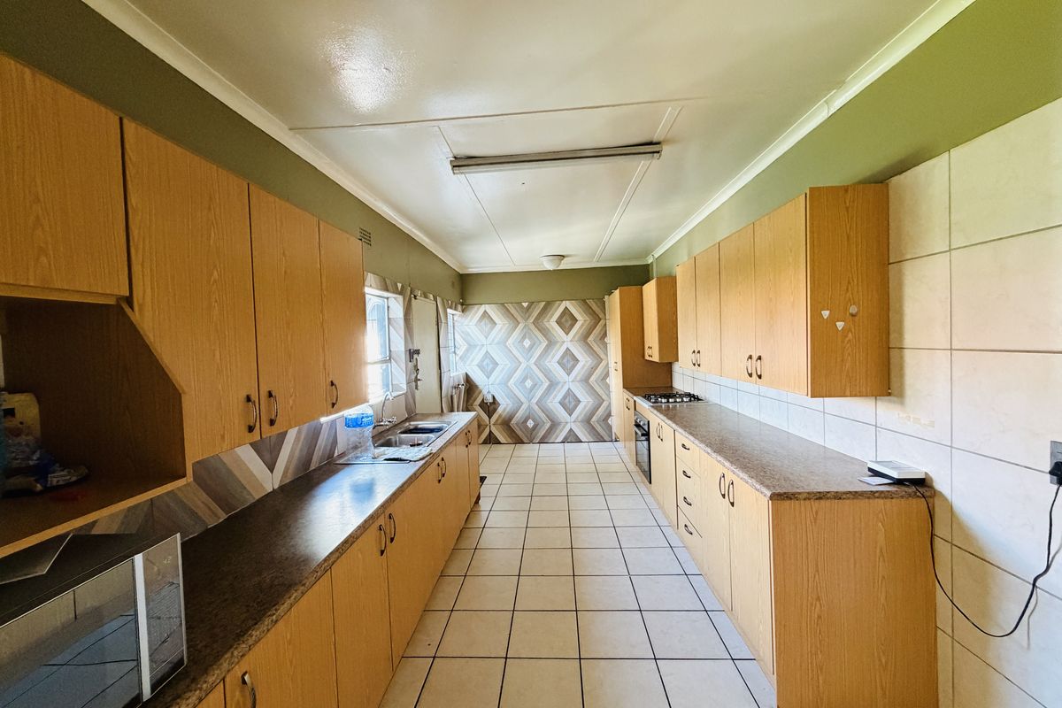 A spacious, functional kitchen featuring extensive laminate cabinetry, laminate countertops, a built-in oven, gas hob, and neutral ceramic floor tiling.