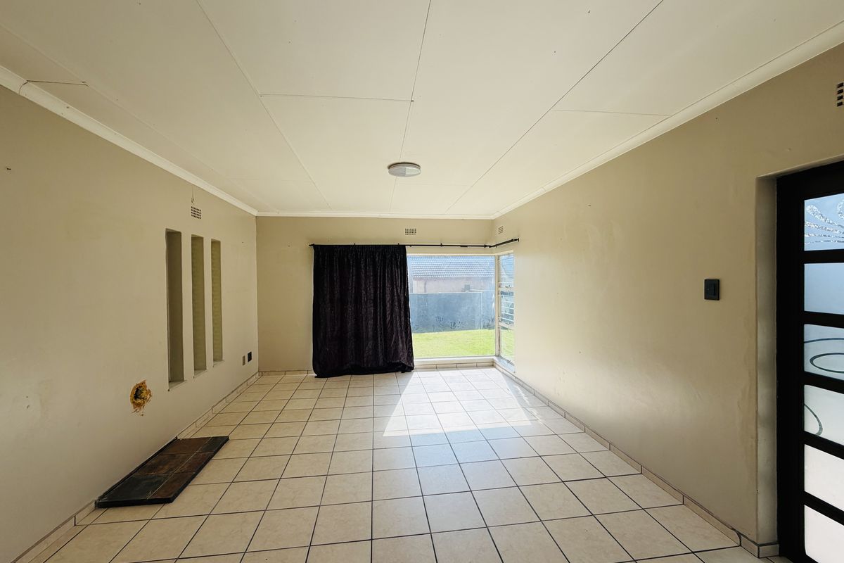 An empty living room featuring tiled flooring, decorative wall niches, and a sliding glass door providing access to the rear garden.