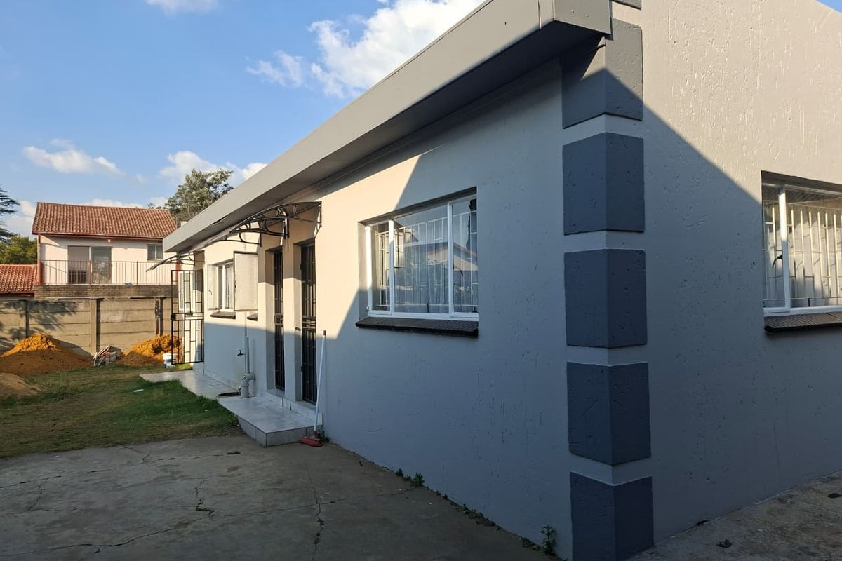 Rear view of the property featuring a grey rendered facade, security bars on windows, and a concrete paved area.