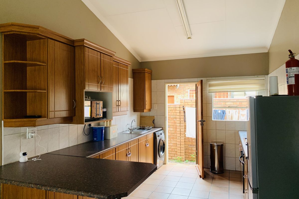 Functional kitchen featuring wooden cabinetry, laminate countertops, tiled backsplash, and integrated laundry plumbing with direct access to an outdoor area.
