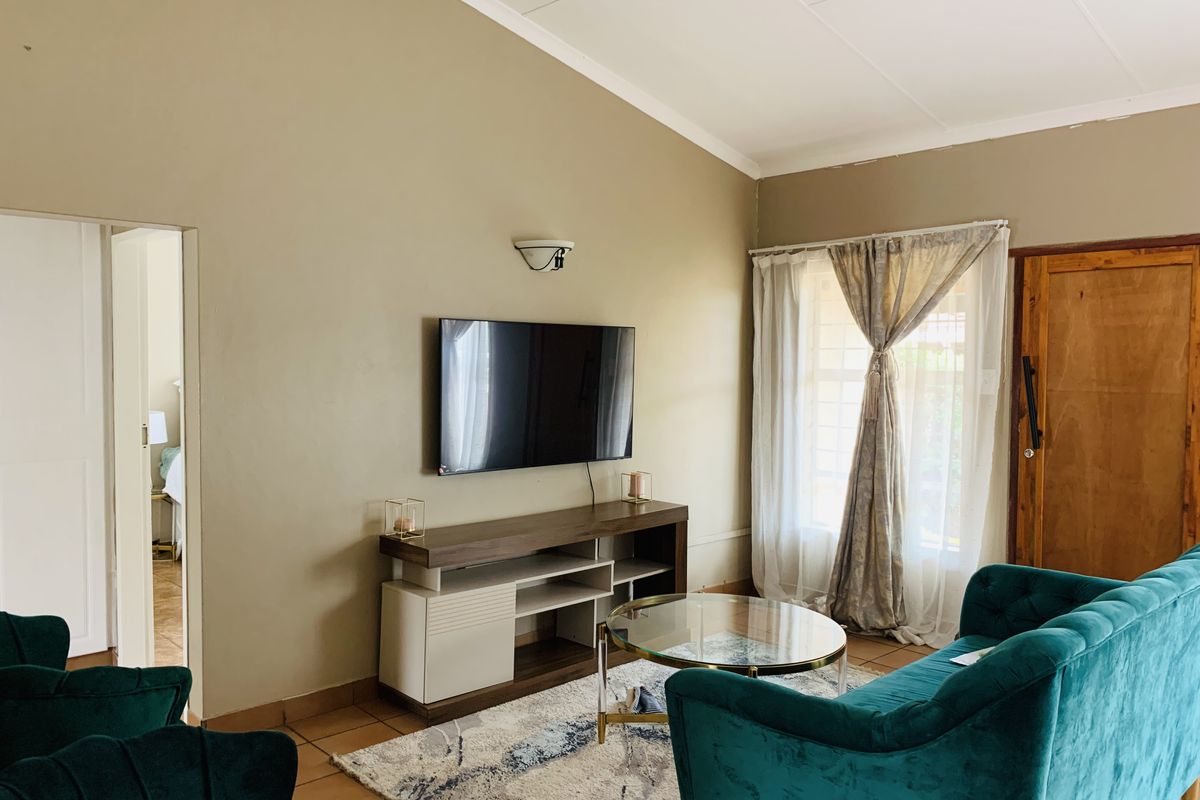A comfortable living room featuring tiled floors, a wall-mounted television, and natural light through a window with security bars.