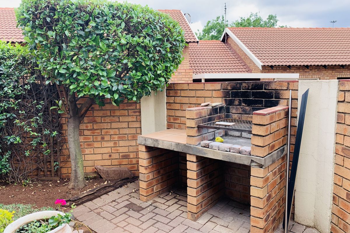 A private rear garden area featuring a built-in brick braai and paved patio space, enclosed by brick boundary walls.