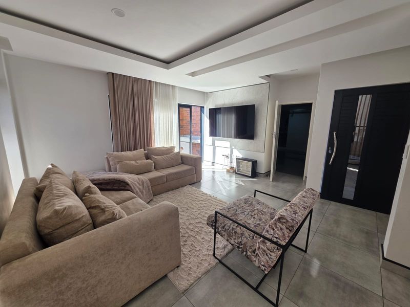 Modern living room featuring tiled flooring, a recessed ceiling design, and a sliding glass door providing natural light.