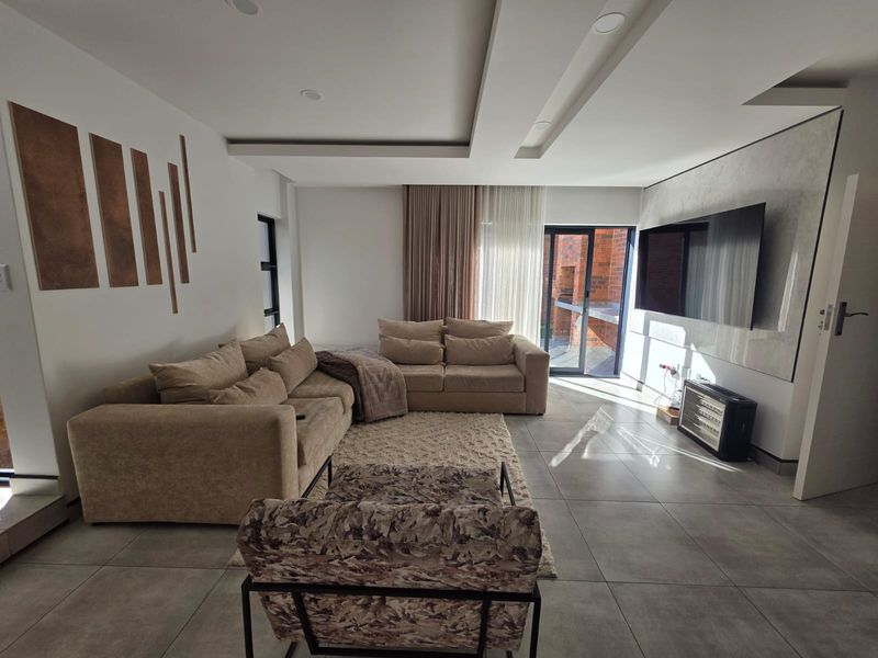 Modern living room featuring large format floor tiles, a recessed ceiling with integrated lighting, and direct access to an outdoor patio area.