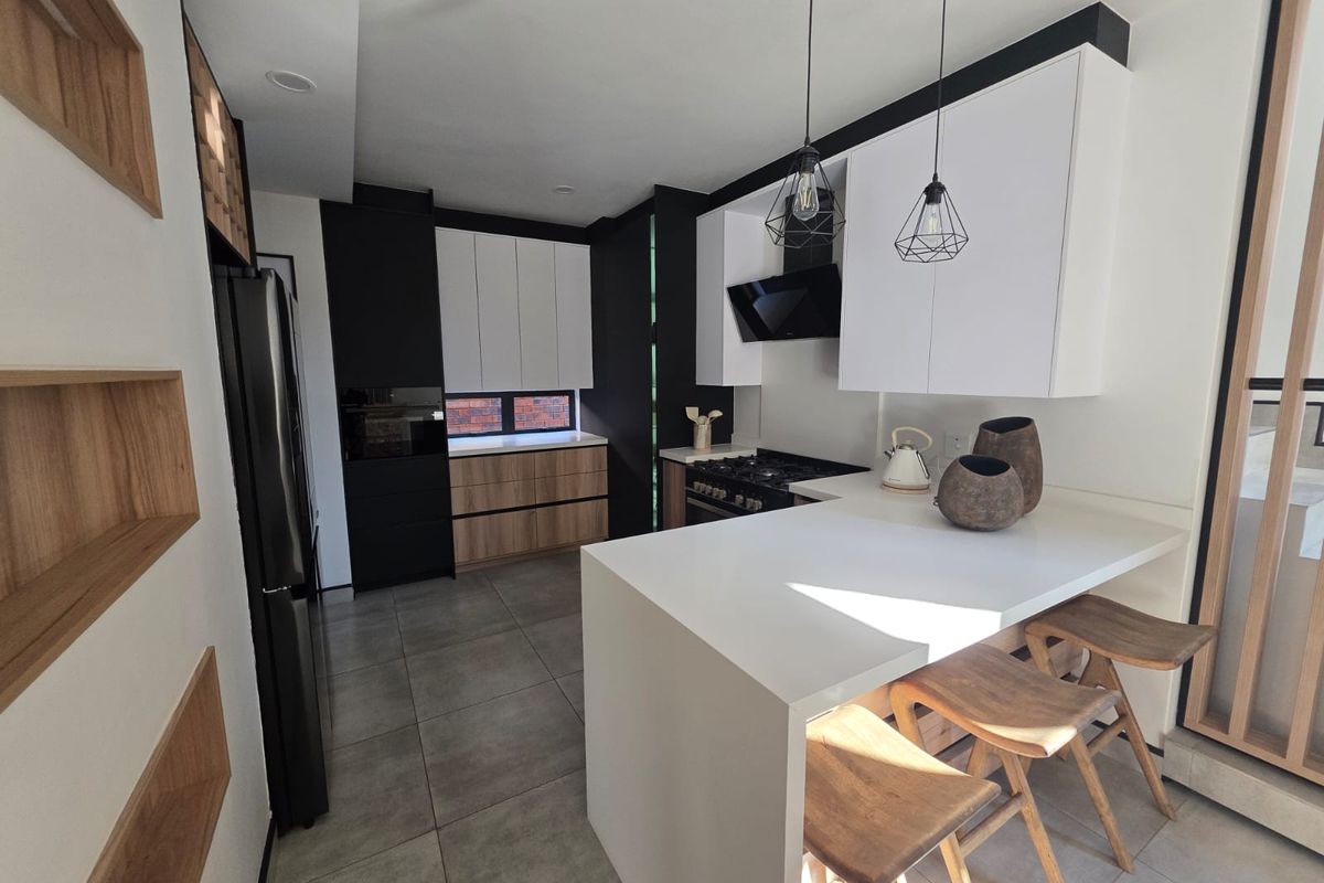 Modern kitchen featuring two-tone cabinetry, stone countertops, integrated appliances, and a functional breakfast bar with contemporary pendant lighting.