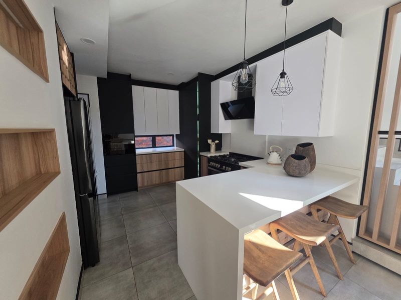 Modern kitchen featuring two-tone cabinetry, stone countertops, integrated appliances, and a functional breakfast bar with contemporary pendant lighting.
