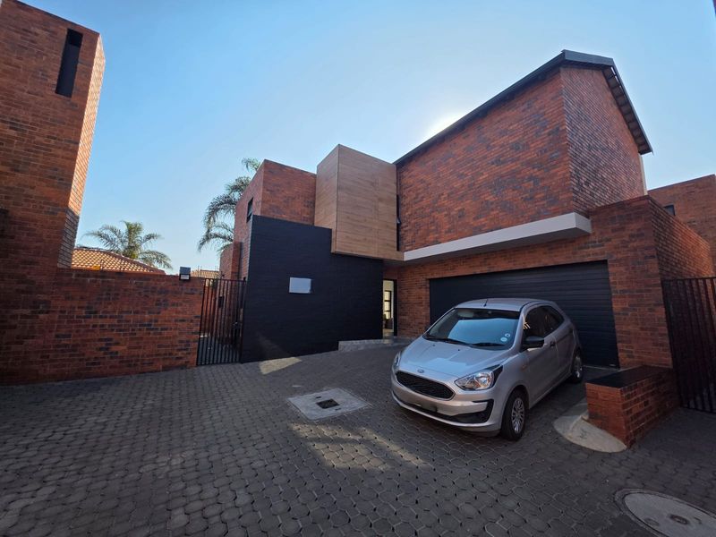 Modern townhouse exterior featuring a striking face brick facade, timber-look accents, and a paved driveway leading to a double garage.