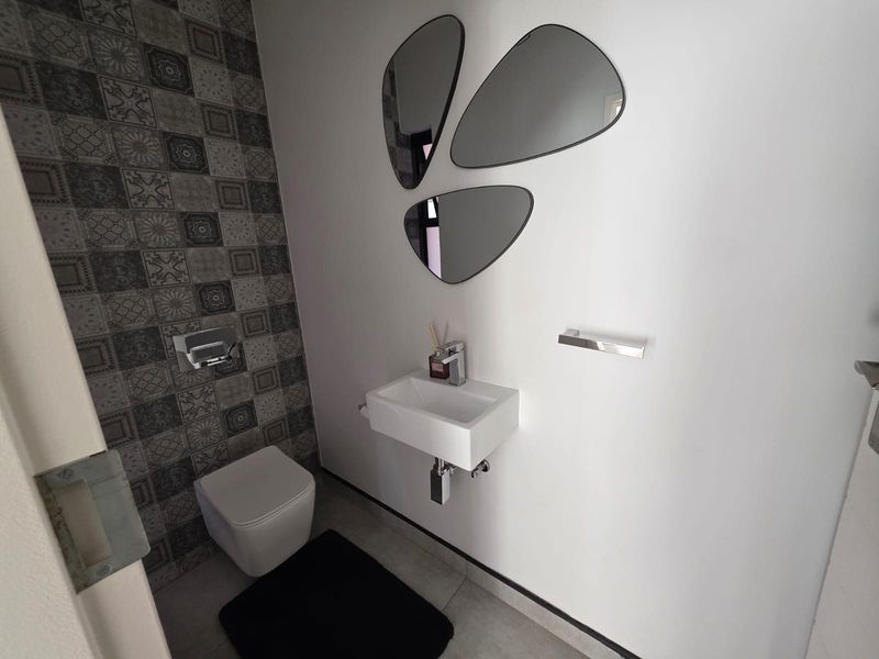 Modern guest cloakroom featuring a wall-mounted basin, wall-hung toilet, and stylish patterned feature tiling.