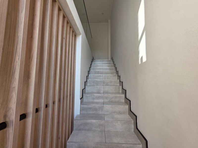 Modern staircase featuring grey tiled steps, a decorative timber slat screen, and a sleek glass balustrade.