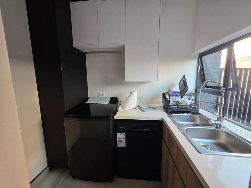 A functional scullery area featuring modern cabinetry, stone countertops, a double stainless steel sink with a gooseneck tap, and dedicated appliance space.