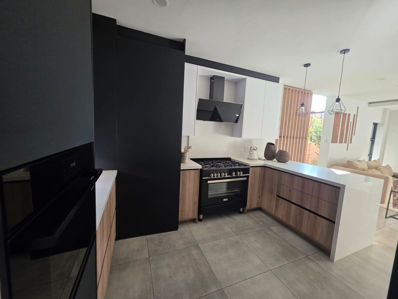 Modern open-plan kitchen featuring sleek two-tone cabinetry, stone countertops, high-end gas cooking appliances, and large format floor tiles, seamlessly flowing into the living area.
