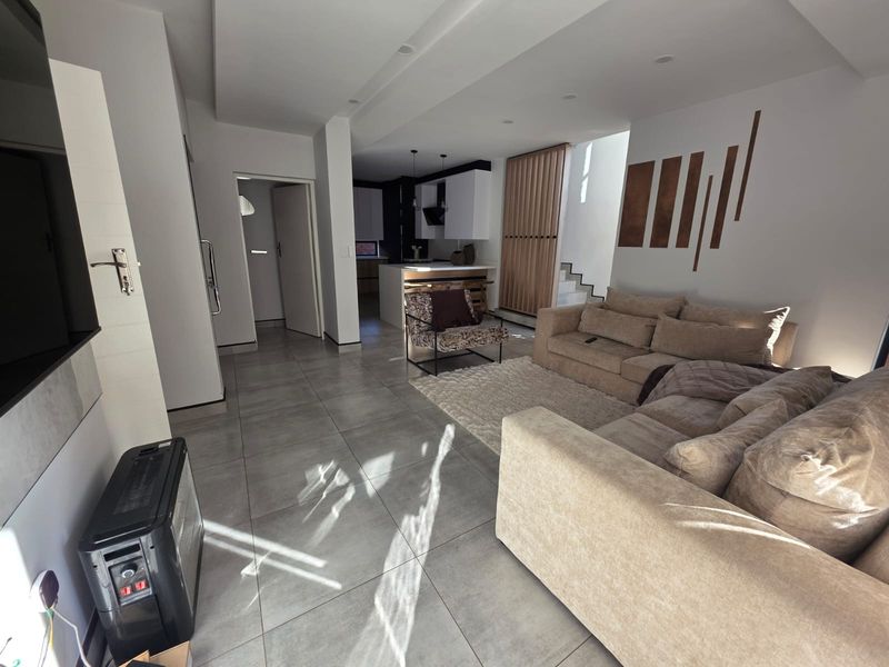 Spacious open-plan living area featuring large format floor tiles, modern kitchen cabinetry, a central island, and a contemporary timber slat staircase feature.