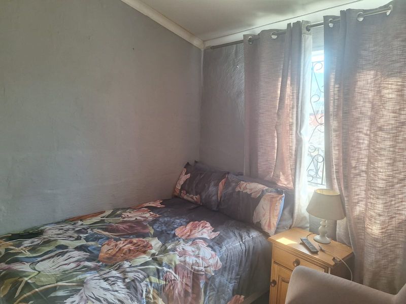 A compact bedroom featuring a window with a security gate and curtain rod, requiring cosmetic updates to the wall finishes.
