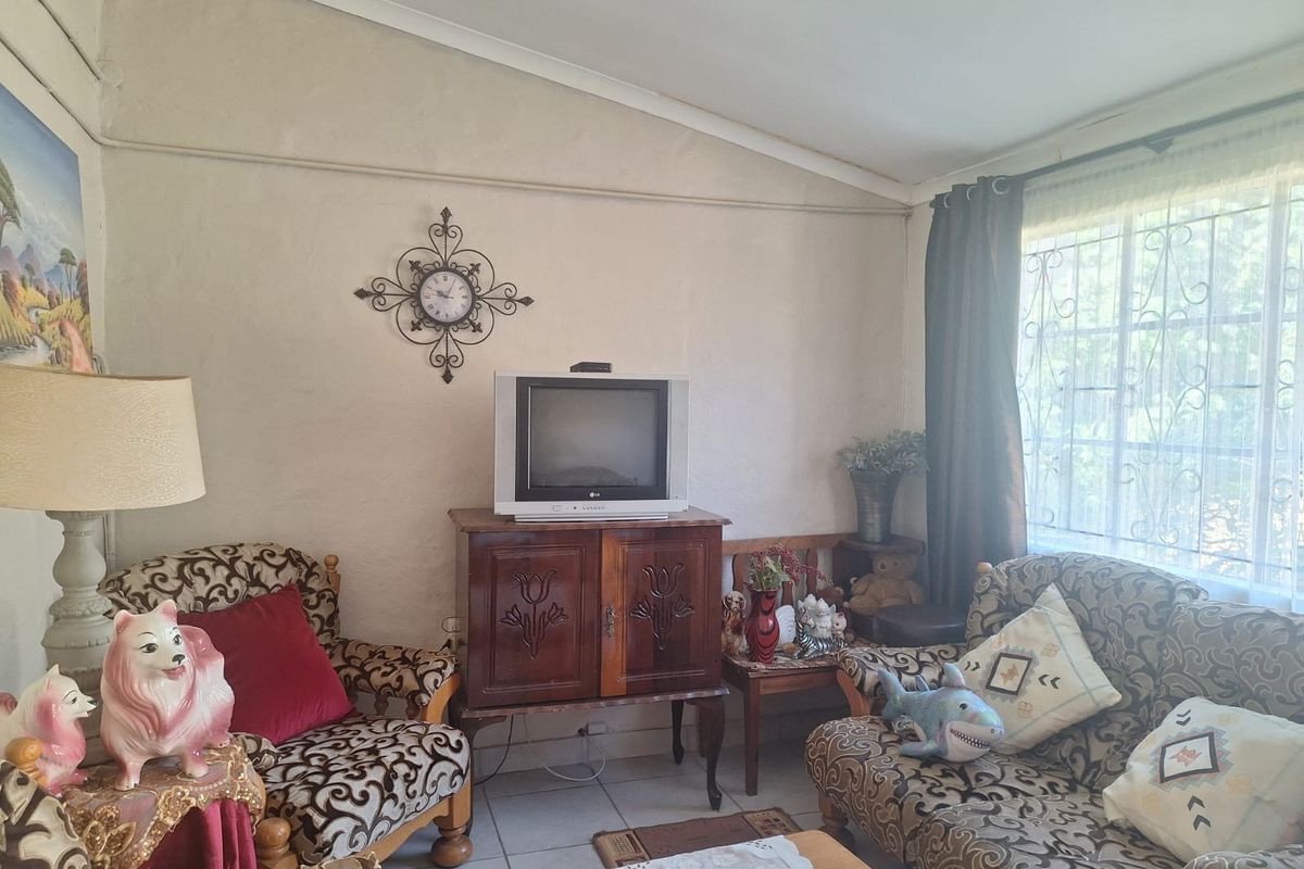 A living room featuring tiled flooring, a sloped ceiling, and a window fitted with security bars.