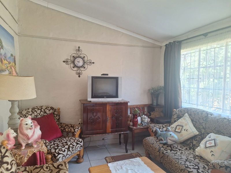 A living room featuring tiled flooring, a sloped ceiling, and a window fitted with security bars.
