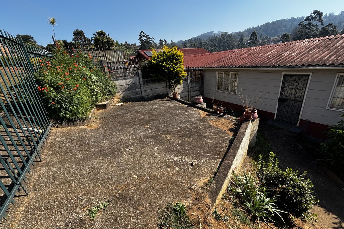 Rear exterior area featuring a concrete paved patio, perimeter security fencing, and retaining wall, offering potential for outdoor landscaping and improvement.