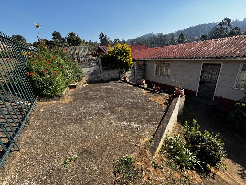 Rear exterior area featuring a concrete paved patio, perimeter security fencing, and retaining wall, offering potential for outdoor landscaping and improvement.