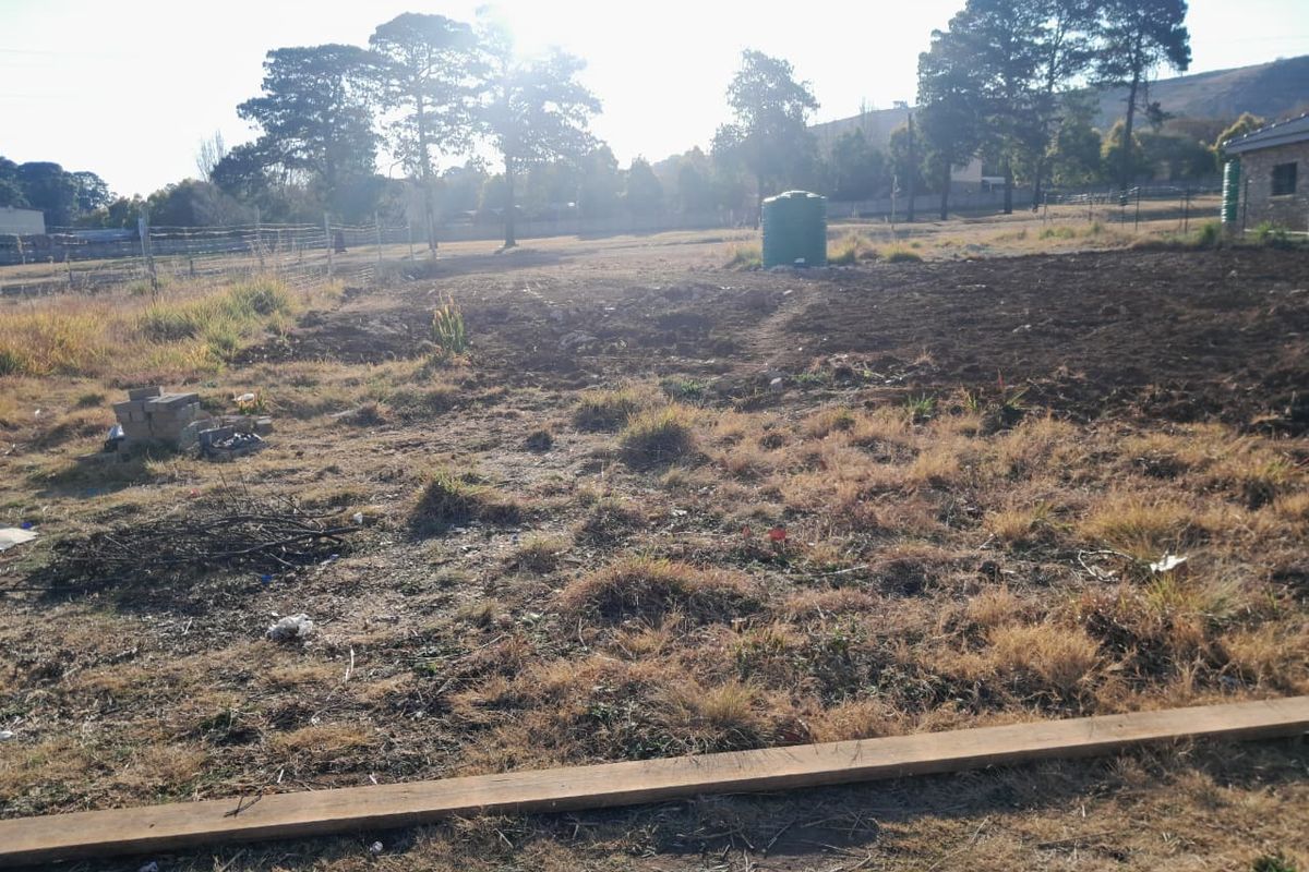 A view of a vacant residential plot featuring natural grass, a water tank, and perimeter wire fencing.
