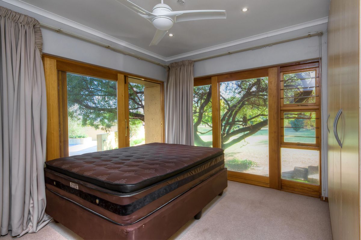 A bedroom featuring large timber-framed windows, built-in cupboards, and a ceiling fan, offering views of the garden.
