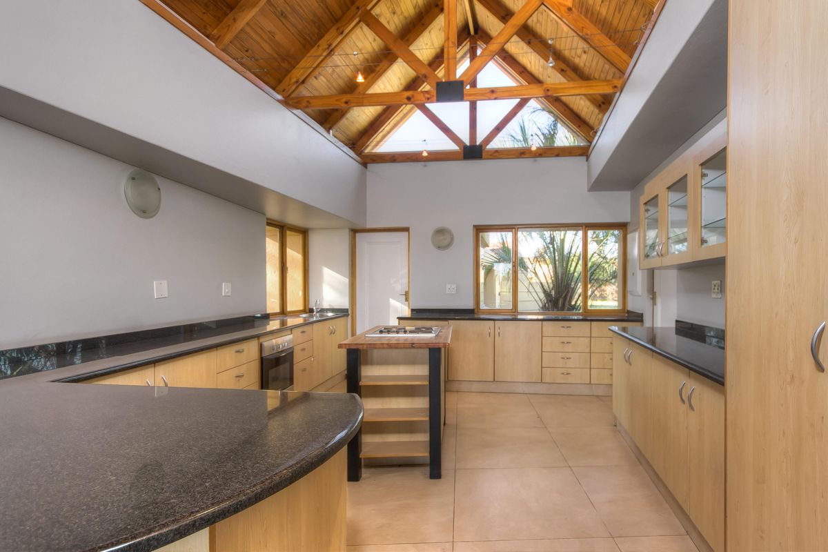 Spacious kitchen featuring light wood cabinetry, dark granite countertops, a central island with a built-in hob, and a striking vaulted timber-truss ceiling.