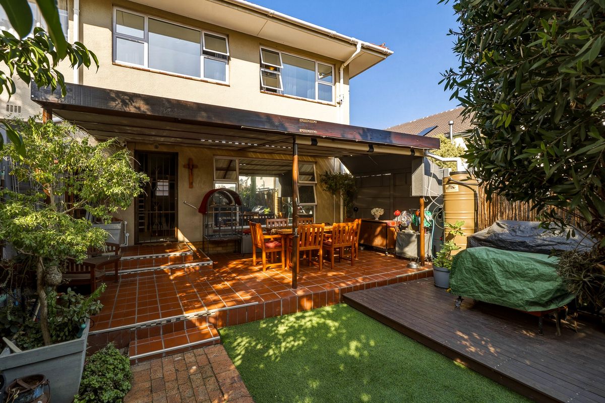 Rear exterior view of the townhouse featuring a tiled patio with a timber pergola, timber decking, artificial lawn, and a water storage tank.