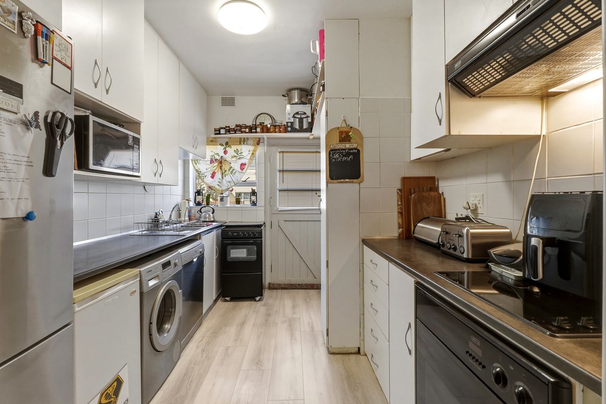 Functional galley-style kitchen featuring white cabinetry, dark laminate countertops, tiled backsplash, and integrated appliances with direct access to the exterior.