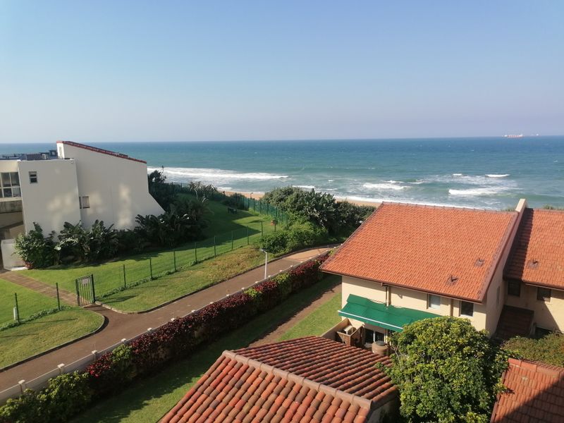Elevated coastal view overlooking the apartment complex grounds, landscaped gardens, and the ocean shoreline.