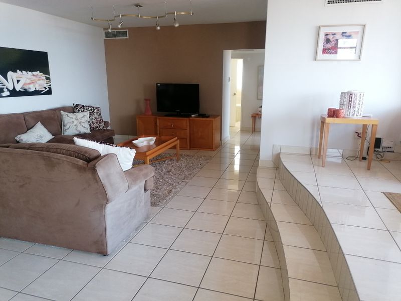 Spacious living area featuring tiled flooring, a raised platform section, and recessed ceiling lighting, providing a functional and open layout.