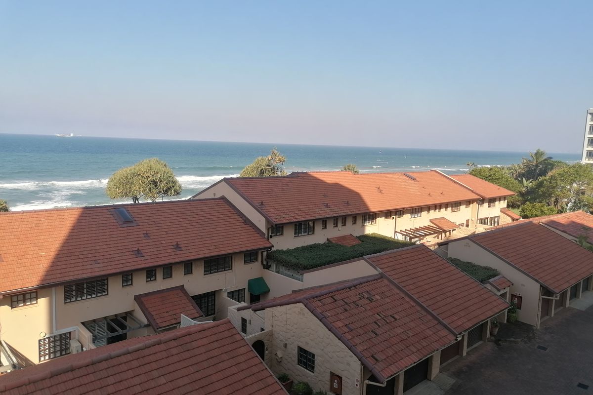 An elevated aerial view of a residential apartment complex featuring terracotta tiled roofs with a direct view of the ocean.