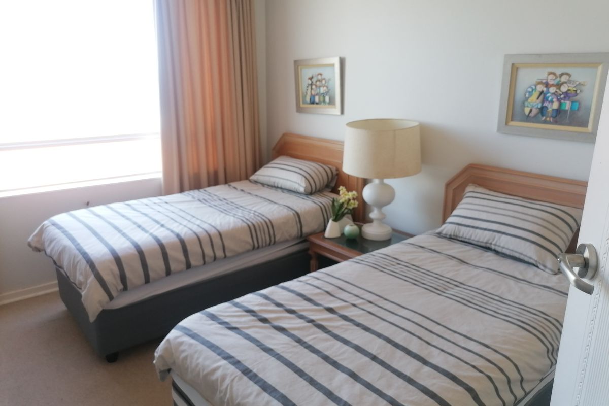 A bedroom featuring a large window with curtains and carpeted flooring, currently configured with two single beds.