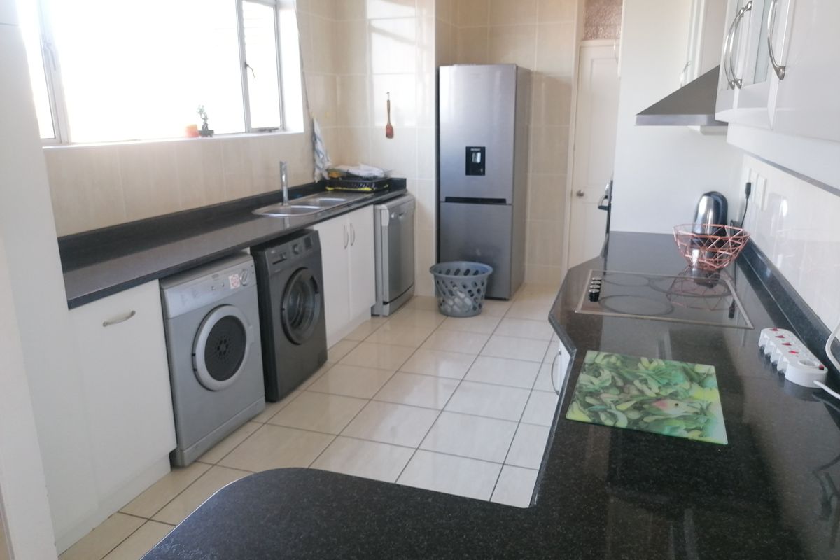 Functional kitchen featuring granite countertops, tiled splashbacks, built-in cabinetry, and an electric hob with extractor fan.