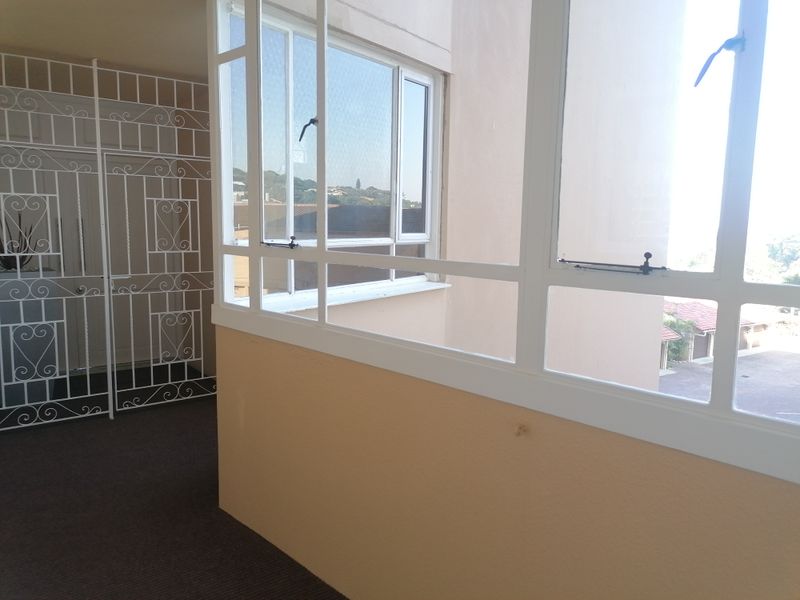 An enclosed balcony or sunroom featuring large aluminium-framed windows, security gate, and neutral wall finishes, offering a bright and versatile additional living space.