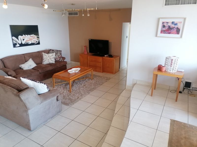 A spacious living room featuring neutral tiled flooring, ducted air conditioning, and track lighting, offering a functional and well-lit living space.