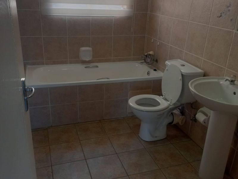 A functional bathroom featuring a built-in bathtub, pedestal basin, and toilet, finished with ceramic wall and floor tiling.