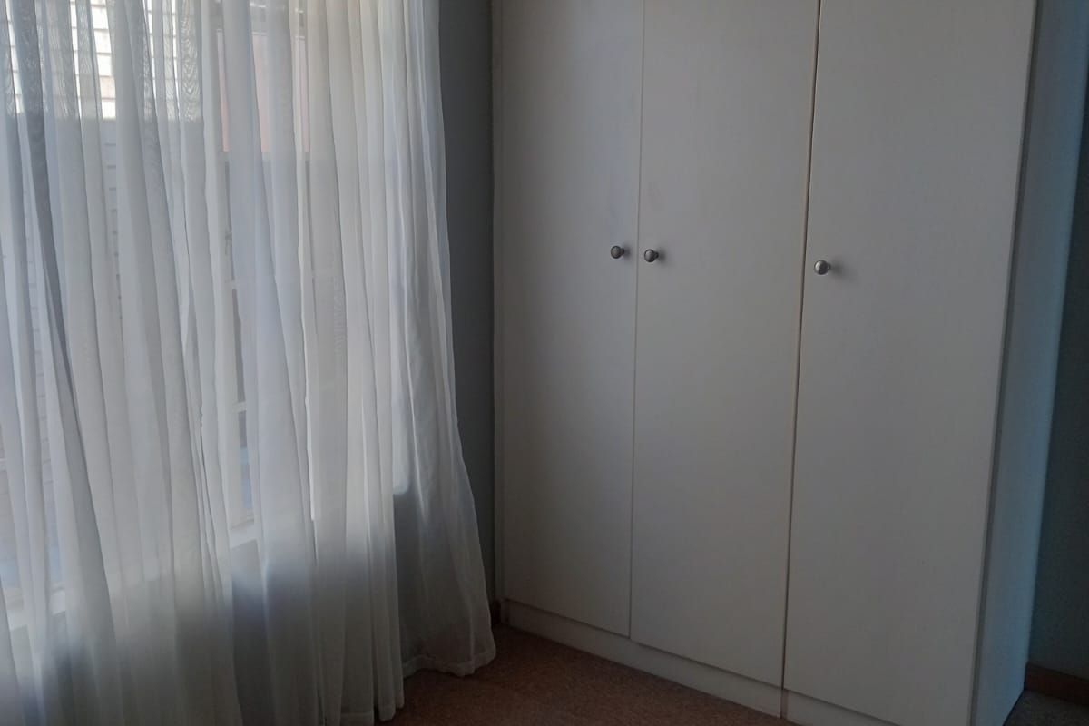 A bedroom featuring neutral carpet flooring, a built-in wardrobe, and a window with sheer curtains.