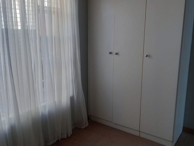 A bedroom featuring neutral carpet flooring, a built-in wardrobe, and a window with sheer curtains.