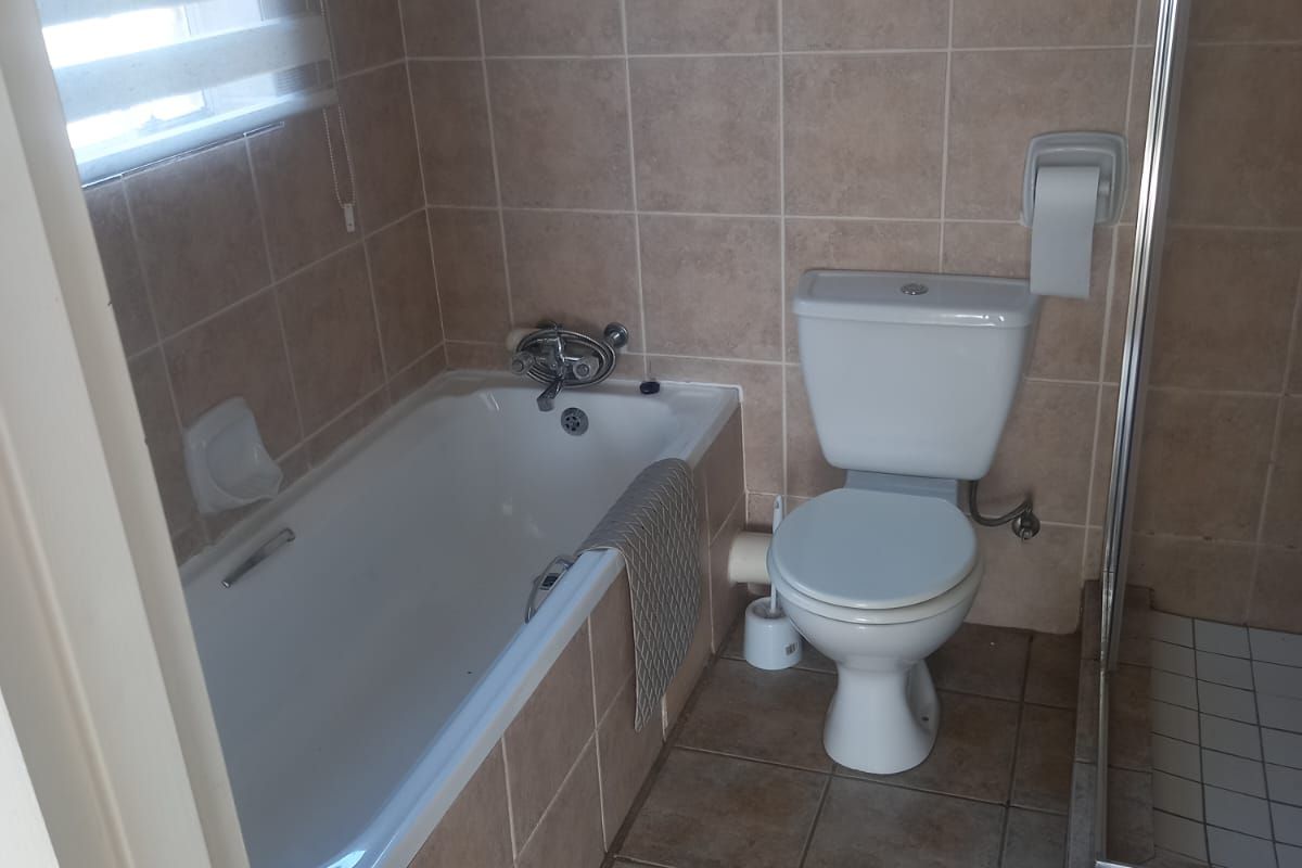 A functional bathroom featuring a bathtub, separate shower enclosure, and toilet with neutral tiled finishes throughout.