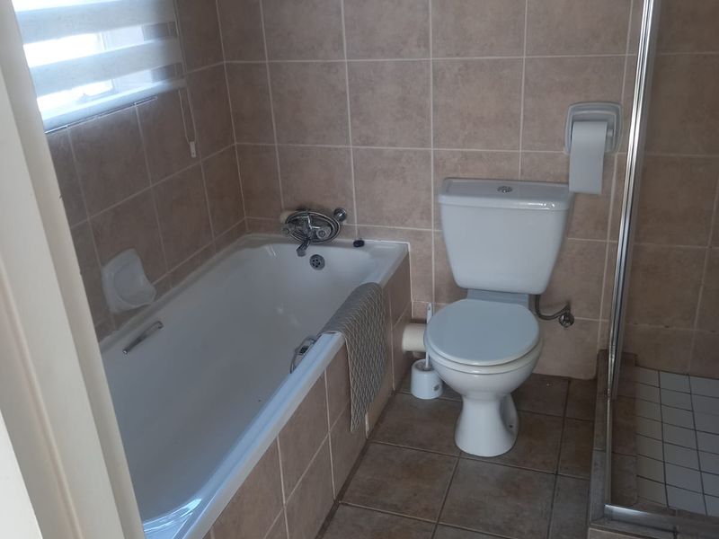 A functional bathroom featuring a bathtub, separate shower enclosure, and toilet with neutral tiled finishes throughout.