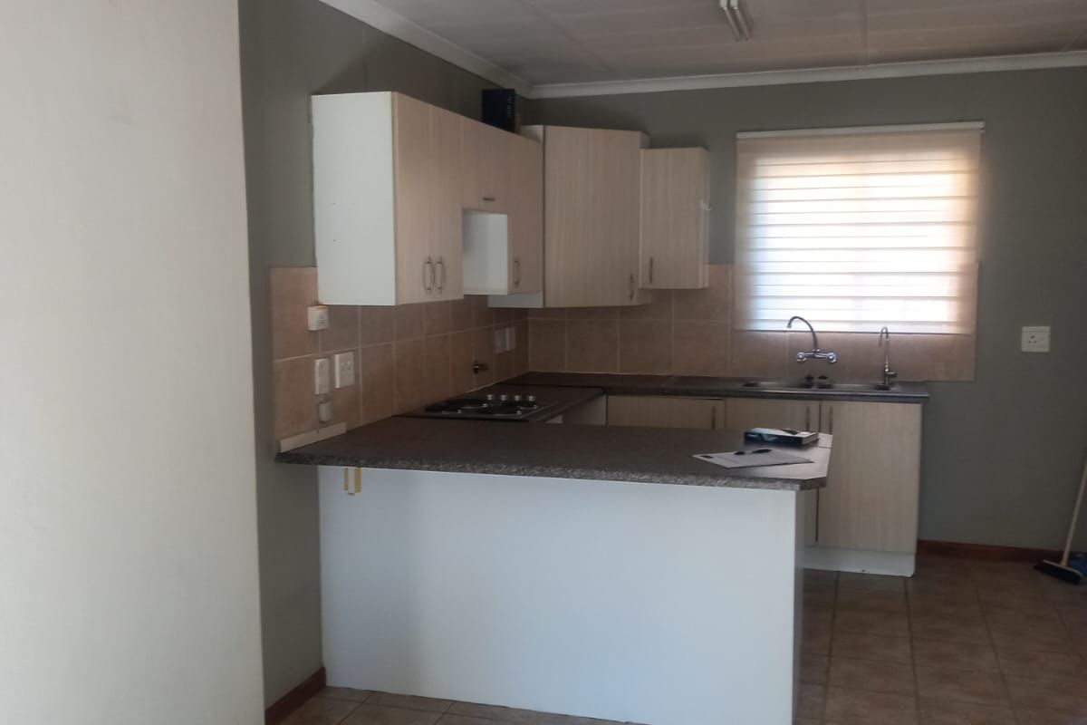 A functional kitchen featuring laminate cabinetry, built-in hob, stainless steel sink, and tiled flooring, offering a practical layout ready for modern updates.